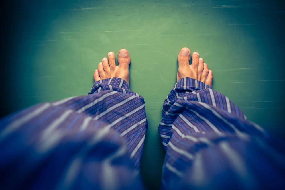 Sleep deprivation at work - Male in pyjama bottoms from the point of view of him looking down at his bare fit